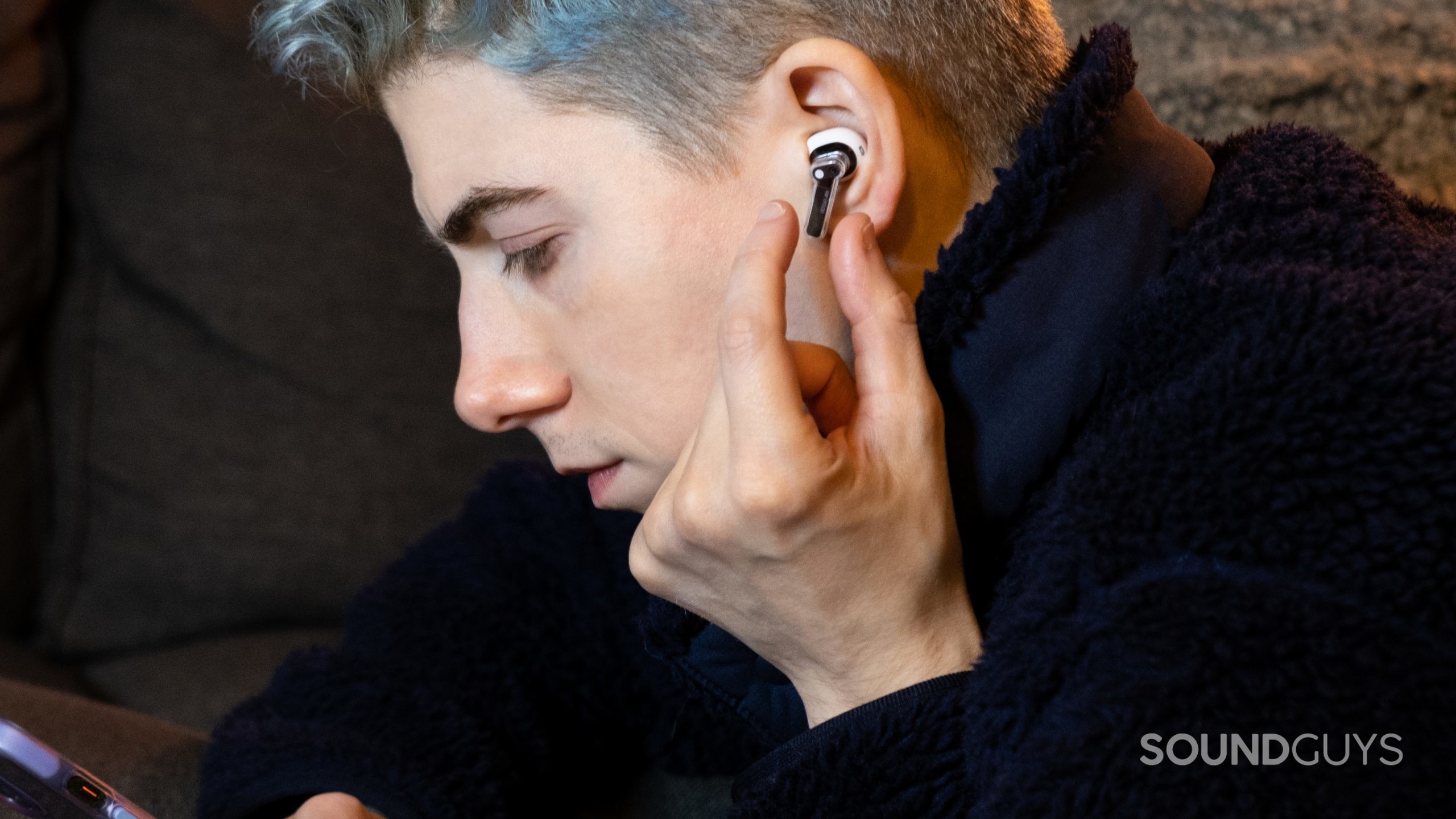 nothing-ear-stick-in-ears A man faces left holding a phone and about to pinch the Nothing Ear (stick).